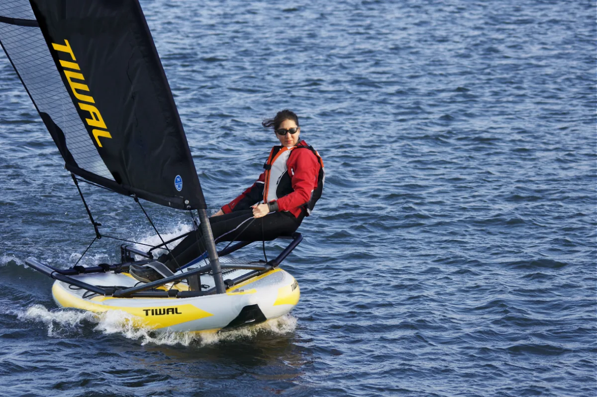 A Tiwal inflatable sailing dinghy under sail with the sailor hiking out, Tiwal branding visible on sail and hull