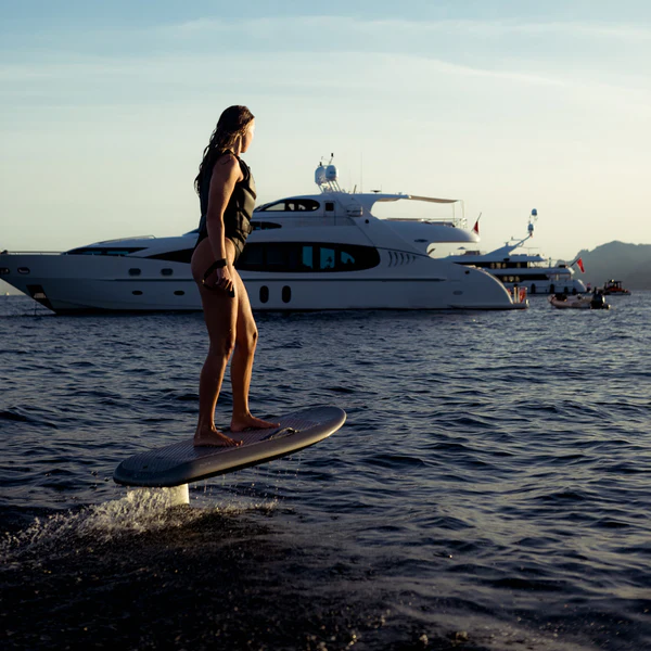 Woman riding an electric hydrofoil board near a superyacht at sunset