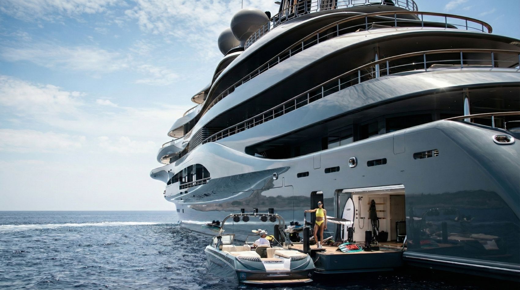 Superyacht at sea with tender alongside, water toys deployed from the swim platform — the operational context where RACLAN and RAMBSS protect