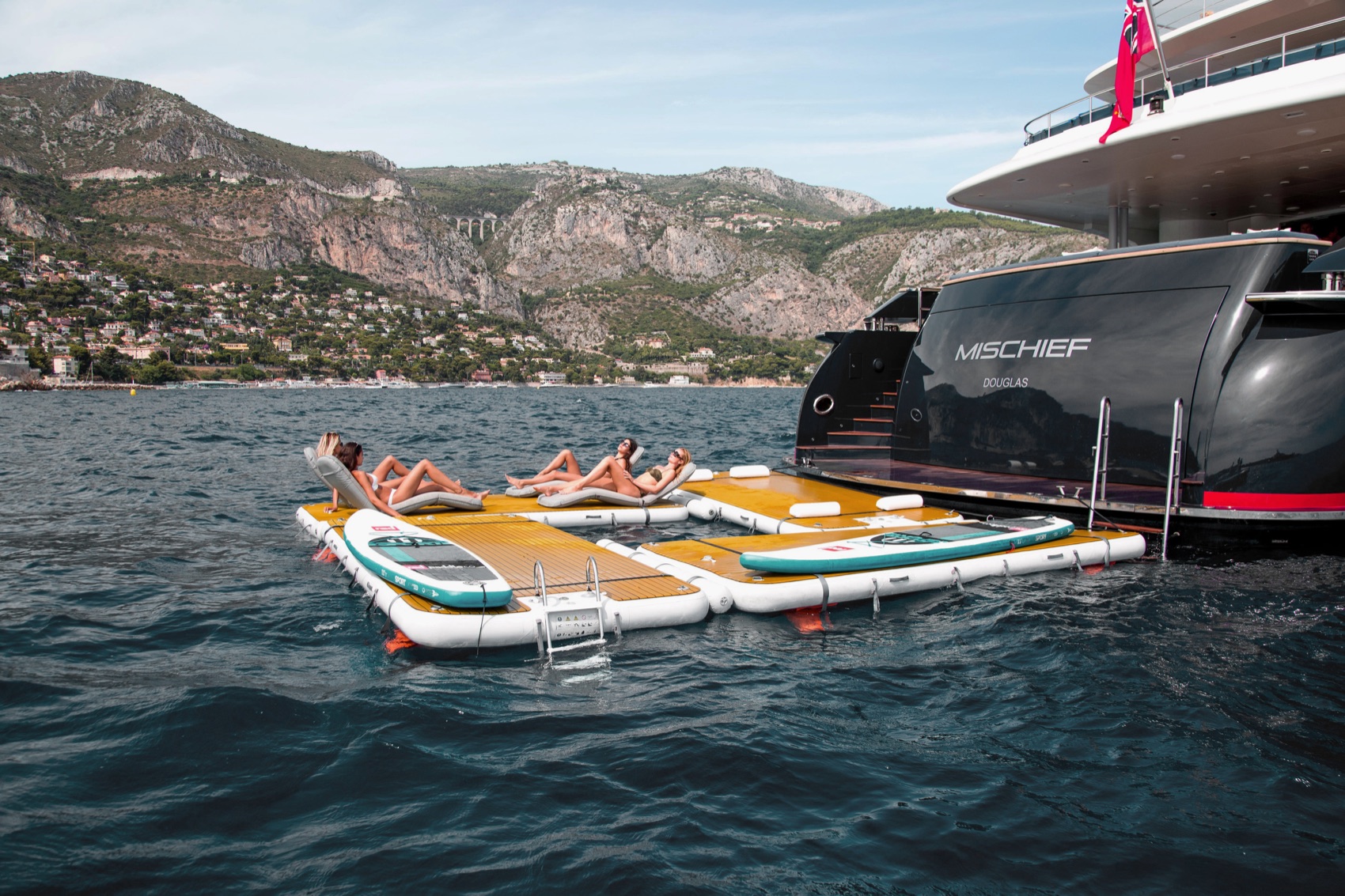 NautiBuoy teak inflatable platform deployed alongside a superyacht with guests