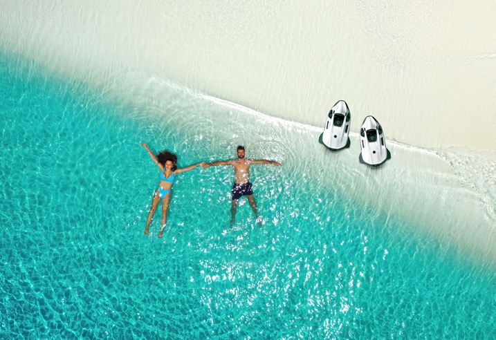 Aerial view of two Seabob units waiting on a tropical beach with owners floating in the shallows &mdash; the end state Mercer Yachting books for ahead of every guest week